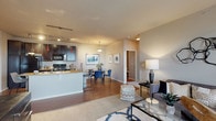 Located at 5101 S Rio Grande St in Littleton, Colorado, this single-floor residence offers a thoughtfully designed open-concept layout that seamlessly connects the kitchen, dining, and living areas. The kitchen is equipped with dark espresso cabinetry, granite countertops, a curved breakfast bar with pendant and track lighting, and black appliances including a full-size refrigerator and range. Adjacent to the kitchen, the dining area accommodates a round glass-top table and is accented by framed artwork, while hardwood-style flooring flows throughout these common areas. The living room features plush carpeting, a sliding glass door, and large windows that fill the space with natural light and provide outdoor views from the private balcony. The layout includes two well-sized bedrooms, each with carpeted floors, large windows, and distinct design character. The primary bedroom benefits from natural light and a warm, neutral palette, while the second bedroom offers a cozy, intimate feel. Two bathrooms serve the residence; one features a full tub-shower combination with tile surround, granite vanity countertop, and hardwood-style flooring. The overall ambiance is modern and cohesive, with neutral tones, contemporary finishes, and a functional floor plan suited for comfortable everyday living.