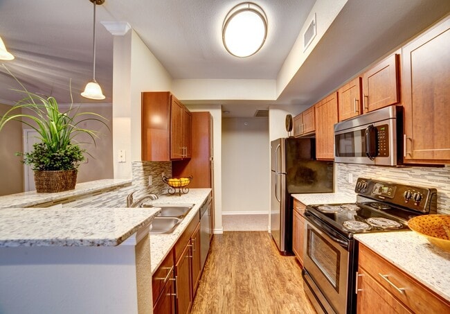Kitchen with chestnut cabinetry, speckled granite countertops, tile backsplash, stainless steel appliances, and hard surface flooring - eaves North Dallas