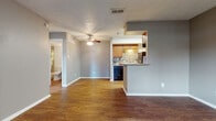 This single-floor residence offers a practical and cohesive layout with consistent design elements throughout. The open-concept living area is anchored by warm hardwood-style flooring that extends seamlessly through the main spaces, complemented by neutral gray walls and crisp white baseboards. A ceiling fan overhead adds both functionality and a finishing touch to the living room, which flows naturally toward the kitchen.

The kitchen features a galley-style configuration with warm wood cabinetry, granite-look countertops, and a striking stacked-stone tile backsplash. Black appliances — including a refrigerator, electric range, and dishwasher — provide a bold contrast to the cabinetry. A peninsula breakfast bar connects the kitchen to the living area, creating an inviting pass-through ideal for casual dining or entertaining.

The bedroom is a comfortable, well-proportioned space with hardwood-style flooring, a ceiling fan, and a window fitted with vertical blinds that allow natural light to filter in. A closet is accessible from within the room, and a hallway leads conveniently to additional storage or utility areas.

The full bathroom includes a tub-shower combination, a single vanity with wood cabinetry, a mirror, and continued hardwood-style flooring. Textured ceilings are present throughout the unit, adding a classic residential character to the overall design.