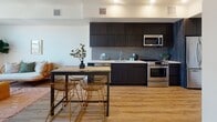 This single-floor residence features a thoughtfully designed open-concept layout that seamlessly integrates the kitchen, dining, and living areas. The kitchen is appointed with dark espresso cabinetry extending to the ceiling, a textured tile backsplash, white quartz countertops, and a full suite of stainless steel appliances, including a range, microwave, and dishwasher. Light wood-tone flooring runs throughout, complementing the clean white walls and creating a warm, cohesive aesthetic.

The dining area sits adjacent to the kitchen, offering a natural transition to the living space beyond. The living room benefits from large windows and a sliding glass door that frame panoramic outdoor views, flooding the space with natural light. A wall-mounted television and access to outdoor scenery make it a functional yet inviting retreat.

Two bedrooms provide comfortable accommodations, each featuring windows with scenic views, including palm trees and city skyline. The bathroom is well-appointed with wood-toned vanity cabinetry, a white countertop with an undermount sink, a large mirror, and a full tub-shower combination clad in grey subway tile. The overall ambiance is clean, modern, and bright throughout.
