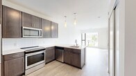 Located at 8001 S Sixth St in Oak Creek, Wisconsin, this one-bedroom, one-bathroom residence offers a thoughtfully designed single-floor layout that maximizes every square foot. The kitchen is a standout feature, showcasing rich dark-stained cabinetry, light quartz-style countertops, a classic white subway tile backsplash, and a full suite of stainless steel appliances including a refrigerator, range, microwave, and dishwasher. Elegant pendant lighting adds a modern touch above the kitchen area. Light wood-tone flooring runs through the main living and kitchen areas, lending warmth and continuity to the space. The entry area is clean and functional, positioned conveniently adjacent to the kitchen. The bedroom features plush carpeting and a large window that frames outdoor views and fills the room with natural light, with direct access to a private balcony overlooking the surrounding greenery. The bathroom offers a clean, minimalist design with matching wood-tone flooring, a shower/tub combination, and a vanity consistent with the home's contemporary aesthetic. Throughout the unit, crisp white walls and modern finishes create a bright, move-in-ready atmosphere suited for comfortable everyday living.