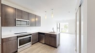 Located at 8001 S Sixth St in Oak Creek, Wisconsin, this one-bedroom, one-bathroom residence offers a thoughtfully designed single-floor layout that maximizes every square foot. The kitchen is a standout feature, showcasing rich dark-stained cabinetry, light quartz-style countertops, a classic white subway tile backsplash, and a full suite of stainless steel appliances including a refrigerator, range, microwave, and dishwasher. Elegant pendant lighting adds a modern touch above the kitchen area. Light wood-tone flooring runs through the main living and kitchen areas, lending warmth and continuity to the space. The entry area is clean and functional, positioned conveniently adjacent to the kitchen. The bedroom features plush carpeting and a large window that frames outdoor views and fills the room with natural light, with direct access to a private balcony overlooking the surrounding greenery. The bathroom offers a clean, minimalist design with matching wood-tone flooring, a shower/tub combination, and a vanity consistent with the home's contemporary aesthetic. Throughout the unit, crisp white walls and modern finishes create a bright, move-in-ready atmosphere suited for comfortable everyday living.