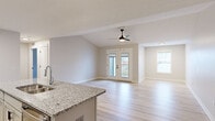 Located at 9924 Cooper Church Dr in Louisville, KY, this well-appointed one-bedroom, one-bathroom unit offers a thoughtfully designed open-concept layout across a single floor. The combined kitchen and living area serves as the heart of the home, featuring light wood-style flooring, vaulted ceilings, and a sleek ceiling fan that enhances the airy ambiance. French doors open to a private balcony, allowing natural light to pour in alongside views of the surrounding neighborhood. The kitchen is a functional standout, equipped with white shaker cabinetry, granite countertops, stainless steel appliances including a range, microwave, and refrigerator, and a central island with a built-in sink — ideal for both cooking and casual dining. The spacious bedroom offers plush carpeting, a ceiling fan, a bright window with outdoor views, and a generous walk-in closet with dual hanging rods for ample storage. The bathroom continues the granite theme with a matching vanity countertop, complemented by light wood-style flooring, a soaking tub, and matte black hardware accents. A dedicated utility room and additional windowed space round out this clean, modern unit.