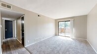 This 1-bedroom, 1-bathroom residence offers a thoughtfully designed single-floor layout that maximizes functionality and comfort. The open living room is bright and welcoming, featuring plush carpet flooring, neutral gray walls, and a sliding glass door that floods the space with natural light and leads to a private outdoor balcony with views of surrounding greenery. A ceiling fan adds to the room's practicality. The layout flows seamlessly into a dedicated dining area and a galley-style kitchen, where dark cabinetry contrasts boldly with light stone countertops. The kitchen is equipped with black appliances, including a range and refrigerator, and features warm hardwood-style flooring that extends throughout the non-carpeted areas. The bedroom is a comfortable retreat, carpeted and naturally lit by a window, with a set of sliding mirrored closet doors providing generous storage. Three closets in total ensure plentiful storage throughout the unit. The bathroom is clean and efficient, featuring a tiled tub-shower combination, hardwood-style flooring, and a wall-mounted light fixture. A connecting hallway ties all rooms together, creating a cohesive and easy-to-navigate floor plan.
