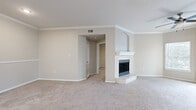 This well-appointed single-story home in Austin, TX offers three bedrooms, two bathrooms, and a thoughtfully designed layout ideal for comfortable everyday living. The living room serves as the heart of the home, featuring plush carpeting, crown molding, a ceiling fan, and a classic white-tiled wood-burning fireplace with a decorative arched alcove above. Sliding glass doors open to a private balcony, allowing natural light to pour in and providing a seamless indoor-outdoor connection. The kitchen is equipped with stainless steel appliances — including a refrigerator, range, and microwave — white cabinetry, and a peninsula island with an undermount sink, offering both functionality and style. Wood-look flooring runs through the kitchen and wet areas. The bedrooms are carpeted and bright, with the secondary bedroom featuring a charming arched window overlooking greenery. The bathrooms are finished with white vanity cabinetry, light countertops, and well-lit mirrors. A dedicated laundry area with shelving provides added convenience. Throughout the home, a neutral warm-beige palette and clean finishes create a cohesive, move-in-ready atmosphere.