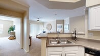 This single-floor residence offers a thoughtfully designed open-concept layout that seamlessly connects the kitchen, dining, and living areas. The kitchen is equipped with stainless steel appliances — including a range, microwave, and refrigerator — complemented by white cabinetry, a peninsula with a double sink, and dark countertops. Rich hardwood-style flooring anchors the kitchen and transitions into plush carpeting throughout the living and bedroom areas. Crown molding adds a polished architectural touch to the main living spaces.

The living room is bright and welcoming, featuring a ceiling fan, soft neutral tones, and a sliding glass door with vertical blinds that opens to an outdoor view. Adjacent to the living area, a dedicated dining nook provides an intimate setting enhanced by a decorative mirror. The primary bedroom is generously sized with a ceiling fan, ample natural light from a large window, and a spacious walk-in closet with full shelving and hanging rods. The bathroom features wood-style flooring, a single-sink vanity with white cabinetry, and a full soaking tub with shower. A dedicated in-unit laundry area houses a full-sized Whirlpool washer and dryer with overhead shelving for added storage convenience.