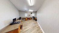 Located on E Slaughter Lane in Austin, Texas, this single-room office space offers a practical and well-organized environment designed for productivity. The room features light wood-style flooring throughout, complemented by neutral gray walls and crisp white baseboards that give the space a clean, modern feel.

A continuous built-in countertop workstation wraps along multiple walls, supported by warm-toned wooden cabinetry with integrated storage below. This L-shaped desk configuration provides generous workspace, accommodating multiple workstations simultaneously — ideal for a small team or multi-use office setup. A bulletin board mounted on the wall serves as a convenient information hub.

Multiple white-framed windows fitted with horizontal blinds allow natural light to fill the room, creating a bright and pleasant working atmosphere. Overhead, a flush fluorescent light fixture provides consistent illumination throughout the day.

The office is accessed through a charming French door with a grid-pane glass panel, adding a touch of architectural character to an otherwise functional space. The entry hallway visible beyond the door suggests connection to a broader facility or building.

Thoughtfully designed for efficiency, this office on Austin's south side offers a comfortable and focused environment suitable for administrative tasks, business operations, or shared workspace needs.