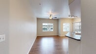 This single-story residence offers a practical and comfortable layout designed for everyday living. The open-concept living area is bright and welcoming, featuring warm wood-look flooring, a textured ceiling, a ceiling fan with light fixture, and multiple windows fitted with horizontal blinds that allow ample natural light to filter in. The space flows seamlessly into the kitchen, which is separated by a peninsula counter with a dark laminate surface. The kitchen is equipped with light wood cabinetry offering generous storage, dark countertops, stainless steel appliances including a refrigerator and over-the-range microwave, a black electric range, and a tall pantry cabinet. Track lighting adds focused illumination to the kitchen area. A hallway connects the main living space to the private areas of the home, where bedrooms feature plush carpeting, ceiling fans, and windows for natural light. One bedroom benefits from a spacious walk-in closet outfitted with built-in shelving and double hanging rods, providing excellent organization. The bathroom includes wood-toned cabinetry and dark countertops. A dedicated in-unit laundry room houses a full-sized washer and dryer alongside a water heater, all set on wood-look flooring. Clean white walls and consistent finishes throughout give the space a cohesive, move-in-ready feel.