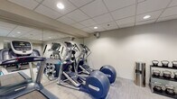 Located at 325 Speen St in Natick, Massachusetts, this fitness center is a well-equipped, single-floor facility designed to support a comprehensive workout experience. The space features a clean, modern aesthetic with neutral-toned walls, a drop-tile ceiling with recessed lighting, and light-colored flooring that creates a bright and welcoming atmosphere.

The cardio area is outfitted with multiple Precor treadmills and elliptical machines, all positioned alongside large wall mirrors that enhance the sense of space and allow users to monitor their form. A dedicated strength training zone includes a multi-functional cable machine suitable for a wide range of exercises, as well as a full rack of dumbbells spanning various weights. A set of kettlebells on a tiered stand provides additional resistance training options.

For functional fitness, the facility offers stability balls, medicine balls, resistance bands, and foam rollers, all neatly organized on a dedicated rack near the windows. Natural light filters in through several windows that offer views of the surrounding greenery, contributing to an energizing environment.

The layout is thoughtfully organized to separate cardio, strength, and functional training zones, making efficient use of the available space. The overall ambiance is clean, professional, and well-maintained, providing users with a focused and comfortable setting for their fitness routines.