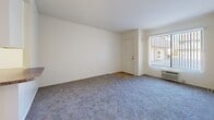 Located at 1668 S Nutwood St in Anaheim, California, this one-bedroom, two-bathroom residence offers a thoughtfully arranged single-floor layout. The combined living room and kitchen area serves as the heart of the home, where plush wall-to-wall carpeting flows through the living space, complemented by a large window with vertical blinds that invites natural light and offers views of the surrounding greenery. A wall-unit air conditioner provides climate control, and a front entry door with an adjacent sidelight window adds to the room's brightness.

The kitchen is well-appointed with white cabinetry, granite-look countertops, a full suite of white appliances including a dishwasher, electric range, and microwave, along with a skylight fixture overhead for added illumination. A breakfast bar peninsula connects the kitchen seamlessly to the living area.

The bedroom is a comfortable retreat featuring soft carpeting, a ceiling fan with light, a window with outdoor views, and a dedicated closet with built-in shelving. The two bathrooms are finished with warm tile flooring; one includes a full tub/shower combination with brushed nickel fixtures. A hallway with vanity connects the living areas to the private spaces, completing the functional and cohesive floor plan.