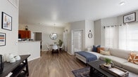 This single-floor residence offers a thoughtfully designed open-concept layout that seamlessly connects the living, dining, and kitchen areas. Rich wood-look flooring flows throughout the main living spaces, creating a warm and cohesive aesthetic complemented by neutral-toned walls and abundant natural light from multiple windows dressed with white blinds and sheer curtains.

The living room is a comfortable gathering space, featuring a large sectional sofa and a corner window arrangement that fills the room with natural light. Adjacent to it, the dining area accommodates a round wooden table beneath a stylish pendant light fixture. The kitchen is well-equipped with warm wood cabinetry, granite countertops, stainless steel appliances, and a peninsula that provides additional prep and serving space. In-unit laundry is also conveniently located nearby.

Both bedrooms are carpeted for added comfort, each featuring a ceiling fan, natural light from windows, and vaulted-style ceilings that enhance the sense of openness. The full bathroom is finished with rich wood vanity cabinetry, granite countertops, wood-look flooring, and a tiled shower-tub combination, completing this functional and inviting home.