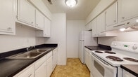 Located at 806 Grandview Pt in Dunbar, West Virginia, this single-floor residence offers a practical and well-organized layout designed for comfortable everyday living. The galley-style kitchen is efficiently arranged with white cabinetry on both sides, dark countertops, a stainless steel sink, and white appliances including a coil-top electric range and a full-size refrigerator. Warm tile-style flooring runs throughout the kitchen, providing a durable and easy-to-maintain surface. A carpeted hallway connects the main living areas, leading to the bedrooms and bathroom. The living area is generously sized, featuring light neutral carpet, a large sliding glass door with vertical blinds that invites natural light, and a ceiling fan. The bedrooms are bright and well-proportioned, each with plush carpeting, windows fitted with blinds offering views of surrounding greenery, and ample closet space — including a walk-in closet in one of the rooms. The full bathroom features tile flooring, a shower-tub combination, and a vanity with counter space. Throughout the residence, white walls and consistent neutral finishes create a clean, cohesive aesthetic that provides a welcoming and move-in-ready atmosphere.