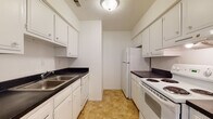 Located at 806 Grandview Pt in Dunbar, West Virginia, this single-floor residence offers a practical and well-organized layout designed for comfortable everyday living. The galley-style kitchen is efficiently arranged with white cabinetry on both sides, dark countertops, a stainless steel sink, and white appliances including a coil-top electric range and a full-size refrigerator. Warm tile-style flooring runs throughout the kitchen, providing a durable and easy-to-maintain surface. A carpeted hallway connects the main living areas, leading to the bedrooms and bathroom. The living area is generously sized, featuring light neutral carpet, a large sliding glass door with vertical blinds that invites natural light, and a ceiling fan. The bedrooms are bright and well-proportioned, each with plush carpeting, windows fitted with blinds offering views of surrounding greenery, and ample closet space — including a walk-in closet in one of the rooms. The full bathroom features tile flooring, a shower-tub combination, and a vanity with counter space. Throughout the residence, white walls and consistent neutral finishes create a clean, cohesive aesthetic that provides a welcoming and move-in-ready atmosphere.
