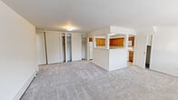 Located at Heatherwood House at Patchogue in Patchogue, NY, this single-floor residence offers a straightforward, functional layout designed for comfortable everyday living. The main living area is generously proportioned, finished with neutral wall-to-wall carpeting that lends a warm, quiet atmosphere throughout. A half-wall partition with a pass-through opening separates the living space from the kitchen, creating a sense of openness while maintaining a distinct boundary between the two areas.

The kitchen is well-appointed with warm-toned wood cabinetry extending along two walls, offering ample upper and lower storage. A skylight overhead fills the space with natural light. White appliances include a refrigerator, dishwasher, electric range, and over-the-range microwave. Light ceramic tile flooring completes the kitchen's clean, practical aesthetic.

The living area features multiple sliding-door closets along one wall, providing substantial built-in storage. Additional rooms include carpeted bedrooms, each with windows that bring in natural light, and at least one room equipped with a wall-mounted air conditioning unit. A full bathroom includes a tub and shower combination with sliding glass doors, a single-sink vanity with a mirrored medicine cabinet, and a clean, white finish throughout.