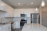 This well-appointed single-floor residence offers a clean, contemporary design throughout. The heart of the home is a thoughtfully designed kitchen featuring crisp white shaker cabinetry, granite countertops, a white subway tile backsplash, and a full suite of stainless steel appliances including a refrigerator, range, microwave, and dishwasher. A central island with a matching granite surface provides additional prep space and casual seating. Wood-look flooring runs through the main living and kitchen areas, complementing the light, neutral color palette found throughout the home. The open living area is bright and airy, with multiple windows dressed in white blinds that allow ample natural light to filter in, and a ceiling fan overhead for year-round comfort. The bedrooms are finished with plush carpet and feature generous closet space, including a spacious walk-in closet equipped with wire shelving on multiple walls for organized storage. The primary bathroom is well-appointed with a dual-sink vanity topped with granite, white shaker cabinetry, brushed nickel hardware, and stylish pendant lighting above a large mirror. A separate tub and shower area features full subway tile surround and brushed nickel fixtures. The overall ambiance is modern, clean, and move-in ready.