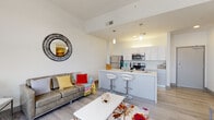 Located on the tenth floor at 325 Park Central East in downtown Springfield, Missouri, this contemporary multi-room unit offers a well-designed open-concept layout with clean lines and a bright, modern aesthetic throughout. Light wood-look flooring flows consistently across the main living areas, complementing the crisp white walls and creating a cohesive, airy atmosphere.

The kitchen serves as a central hub of the space, featuring white cabinetry, light quartz countertops, stainless steel appliances including a refrigerator, range, and microwave, and a peninsula island with seating for two. Pendant lighting anchors the kitchen and living areas, adding warmth to the open floor plan. The living room benefits from oversized windows that frame elevated views of the surrounding cityscape, filling the space with abundant natural light.

Two bedrooms are each equipped with large windows offering city views, providing a bright and comfortable retreat. Both bathrooms mirror each other in design, featuring gray vanity cabinetry, light tile flooring, and clean, minimalist fixtures. The overall layout is efficient and thoughtfully organized, making strong use of the available space while maintaining an uncluttered, contemporary feel throughout.