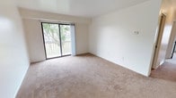 This single-floor residence offers a clean, functional layout spread across several well-defined spaces. The living room serves as the centerpiece of the unit, featuring neutral wall-to-wall carpeting, white walls, and a large sliding glass door that opens directly onto a private balcony. The balcony overlooks a spacious, tree-lined green space with views of surrounding buildings, providing a pleasant outdoor retreat. Natural light flows generously through the sliding door, contributing to an open and airy atmosphere.

The kitchen is efficiently arranged in an L-shaped configuration, offering ample wood-toned cabinetry for storage, light-colored countertops, a stainless steel sink, a dishwasher, and space for additional appliances. Wood-look flooring adds warmth and practicality to this area.

The bedrooms are carpeted and bright, each featuring windows that frame views of the surrounding greenery. The neutral tones and clean lines throughout create a versatile canvas suitable for various décor styles.

The bathroom is finished with wood-look flooring, a full-size tub and shower with white tile surround, a toilet, and a white vanity with a sink, all maintained in a clean, straightforward layout. Overall, the unit presents a practical and comfortable living environment.