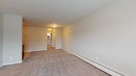 This single-floor unit offers a practical and comfortable layout designed to maximize livable space. The open-concept living and kitchen area serves as the heart of the home, with plush wall-to-wall carpeting in the living space transitioning to tile flooring in the kitchen. Large windows allow natural light to fill the living area, creating a bright and welcoming atmosphere, while a wall-mounted air conditioning unit and baseboard heaters ensure year-round comfort.

The kitchen is equipped with rich warm-toned wood cabinetry, light granite-style countertops, a stainless steel sink, and a black gas range with an overhead ventilation hood, offering both style and functionality. Ample cabinet storage makes the space as practical as it is attractive.

The bedrooms are generously sized, each featuring soft carpeting, neutral wall tones, and baseboard heating. Closet access is conveniently located within or adjacent to the sleeping areas.

The bathroom is thoughtfully finished with stone-look tile flooring, a white vanity with an oversized mirror, a well-lit vanity strip light, a window for natural ventilation, and a tiled shower surround with a decorative mosaic accent strip, lending a clean and polished aesthetic throughout.