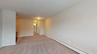 This single-floor unit offers a practical and comfortable layout designed to maximize livable space. The open-concept living and kitchen area serves as the heart of the home, with plush wall-to-wall carpeting in the living space transitioning to tile flooring in the kitchen. Large windows allow natural light to fill the living area, creating a bright and welcoming atmosphere, while a wall-mounted air conditioning unit and baseboard heaters ensure year-round comfort.

The kitchen is equipped with rich warm-toned wood cabinetry, light granite-style countertops, a stainless steel sink, and a black gas range with an overhead ventilation hood, offering both style and functionality. Ample cabinet storage makes the space as practical as it is attractive.

The bedrooms are generously sized, each featuring soft carpeting, neutral wall tones, and baseboard heating. Closet access is conveniently located within or adjacent to the sleeping areas.

The bathroom is thoughtfully finished with stone-look tile flooring, a white vanity with an oversized mirror, a well-lit vanity strip light, a window for natural ventilation, and a tiled shower surround with a decorative mosaic accent strip, lending a clean and polished aesthetic throughout.