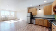 Located at 1440 Independence St in Lakewood, Colorado, this single-floor residence offers a well-designed layout that balances functionality and modern style. The open-concept living and kitchen area serves as the heart of the space, filled with natural light streaming through windows that overlook the surrounding neighborhood. Light wood-style flooring runs throughout, creating a warm and cohesive aesthetic.

The kitchen is thoughtfully appointed with warm-toned maple cabinetry extending to the upper walls for ample storage, dark countertops, and a full suite of stainless steel appliances including a refrigerator, dishwasher, range, and microwave. A green tile backsplash adds a pop of color and visual interest, while a pendant light fixture overhead provides focused task lighting. The entry door, finished in a bold green, adds a distinctive architectural accent.

The bathroom features a full tub and shower combination with clean white surroundings and wood-style flooring, offering a crisp and practical design. The bedroom is a quiet, sunlit retreat with a window framing outdoor views, smooth walls, and rich dark wood-style flooring that grounds the room. The overall layout, as seen in the floorplan, is compact yet efficiently organized, making excellent use of every area within the space.