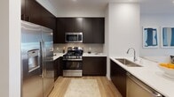 This single-story residence at The Grove in Piscataway, New Jersey offers a well-appointed one-bedroom, one-bathroom layout designed with a clean, contemporary aesthetic. The interior features warm wood-tone flooring that runs throughout the main living areas, connecting each space cohesively.

The kitchen is outfitted with dark espresso cabinetry extending to the ceiling, light quartz countertops, a tile backsplash, and a full suite of stainless steel appliances including a gas range, microwave, refrigerator, and a deep undermount sink — providing both functionality and a polished visual contrast.

The living area presents a bright, neutral backdrop well-suited for modern furnishings, with recessed lighting and ample wall space for artwork and décor.

The bedroom is a serene retreat featuring large windows dressed with sheer curtains and roller shades that allow natural light while maintaining privacy. A walk-in closet offers organized storage, and a dedicated vanity area adds practical convenience.

The full bathroom is finished with large-format light tile flooring, a dark espresso vanity with a wide mirror, and a full shower-tub combination with a curved curtain rod, maintaining the home's consistent modern palette throughout.