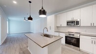 Located at 201 Hills Rd in Panama City Beach, FL, this well-designed one-bedroom, one-bathroom residence offers a clean, modern aesthetic throughout its thoughtfully arranged single-floor layout. Light wood-look flooring flows seamlessly through every room, complemented by crisp white walls, crown molding, and bright natural light.

The open-concept kitchen and living area serves as the heart of the home. The kitchen is outfitted with tall white shaker-style cabinetry, dark hardware accents, a subway tile backsplash, stainless steel appliances including a refrigerator, range, and microwave, and a central island with a quartz-style countertop and an undermount sink, illuminated by stylish black pendant lights. The adjacent living area is spacious and airy, featuring a ceiling fan and ample room for furnishings.

The bedroom is generously sized, filled with natural light from a trio of windows, and includes a ceiling fan and direct access to a walk-in closet equipped with wire shelving systems for organized storage. French doors open to a private outdoor balcony with wood decking and metal railings, offering pleasant community views.

The full bathroom features white cabinetry, a dark countertop, black hardware details, a full tub-shower combination, and matching light wood flooring, maintaining the home's cohesive modern design throughout.