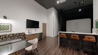 Located at 231 12 Ave SE in Calgary, this golf simulator suite offers a well-appointed, single-floor layout designed to blend sport and hospitality. The space is divided into three functional zones: the simulation bay, a lounge and dining area, and an entry/equipment zone.

The simulation bay is enclosed in a dark, blackout environment with a large projection screen and artificial turf hitting surface, providing an immersive golf experience. Track lighting overhead illuminates the bay precisely, while the surrounding dark walls and curtains maximize screen visibility.

Adjacent to the bay is a stylish lounge area anchored by a marble-topped bar counter with leather-upholstered bar stools. Dark wood paneling along the counter base contrasts cleanly with the white quartz surface. A wall-mounted flat-screen TV is positioned above a wood-grain kitchenette equipped with a sink, under-counter refrigerator, and ample cabinetry. A seating area with a dark table and upholstered chair completes the lounge.

The entry zone features a reception-style counter with storage for golf bags and clubs, wall-mounted artwork, and bench seating. Rich hardwood-style flooring flows throughout, complemented by soaring ceilings with crisp white walls. The overall ambiance is modern, upscale, and purpose-built for private golf entertainment.