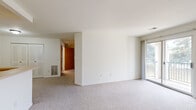 This single-floor unit offers a clean, functional layout with a neutral color palette throughout. The living area is generously proportioned, featuring wall-to-wall carpeting and white walls that create a bright, open atmosphere. A sliding glass door leads directly to a private balcony, providing outdoor views of surrounding greenery and filling the room with natural light. A floor-mounted HVAC vent ensures year-round climate control.

The kitchen is efficiently designed with white cabinetry, a gas range, refrigerator, and dishwasher. A peninsula with a built-in sink separates the kitchen from the living area, offering additional counter space and casual dining potential. Durable stone-look tile flooring runs throughout the kitchen, adding a practical and visually grounding contrast to the carpeted living spaces.

The bedroom is a comfortable, carpeted room with a window fitted with blinds, a wood-tone entry door, and a dedicated closet equipped with wire shelving for organized storage.

The full bathroom features the same stone-look tile flooring as the kitchen, a combined tub and shower with a chrome curtain rod and grab bars, a toilet, and a vanity with a countertop sink. The unit also includes an electrical panel conveniently located within the kitchen area.