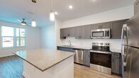 Located at 1191 W Price Blvd in North Port, Florida, this well-appointed one-bedroom, one-bathroom unit offers a thoughtfully designed open-concept layout. Light wood-style flooring flows seamlessly throughout the living areas, creating a warm and cohesive aesthetic.

The kitchen is a standout feature, boasting a large granite-topped island with pendant lighting above, gray shaker-style cabinetry, a white subway tile backsplash, and a full suite of stainless steel appliances including a range, microwave, dishwasher, and refrigerator. Recessed lighting and generous counter space make this kitchen as functional as it is attractive.

The living area is bright and open, flowing naturally from the kitchen and offering ample room for everyday living. The bedroom features a ceiling fan, a sizable closet with bi-fold doors, and a window that lets in natural light with views of the outdoors. Additional storage is accessible via a louvered closet door near the entryway.

The bathroom is finished with large-format neutral floor tiles, a dark-toned vanity with a granite countertop, and safety grab bars, reflecting an accessible and practical design. Clean white walls and crisp trim throughout the unit contribute to an overall fresh and modern ambiance.