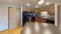 This single-floor, 2-bedroom, 2-bathroom residence offers a well-designed layout that balances comfort and functionality. The kitchen is outfitted with warm honey-toned cabinetry, dark granite-style countertops, a full suite of black appliances including a refrigerator, range, and microwave, and light hardwood flooring. A peninsula counter provides additional workspace and a casual dining surface. Both bedrooms are generously sized, featuring plush wall-to-wall carpeting, neutral warm-toned walls, and individual windows that bring in natural light and outdoor views. Baseboard heating runs along the perimeter of each bedroom for efficient climate control. The primary bathroom includes a wide vanity with a light stone-style countertop, warm wood cabinetry, and an adjacent walk-in closet equipped with wire shelving for ample storage. A second full bathroom conveniently incorporates an in-unit laundry area with a full-sized washer and dryer, adding everyday practicality. Consistent warm wood trim and neutral tones throughout the unit create a cohesive and inviting ambiance. The thoughtful floor plan, visible in the dollhouse view, ensures a smooth flow between living, dining, and private spaces.