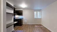 Located at 3635 Phinney Ave N in Seattle's vibrant Phinney Ridge neighborhood, Unit 6 is a thoughtfully designed studio that maximizes every inch of its single-floor layout. The open living area features warm-toned laminate wood flooring that runs throughout, creating a cohesive and inviting atmosphere. Neutral white walls keep the space feeling bright and airy, complemented by a window that brings in natural light.

The kitchenette is outfitted with dark espresso cabinetry, light countertops, and a suite of black appliances including a full-size refrigerator, over-the-range microwave, and an induction cooktop. Under-cabinet lighting adds a modern touch and enhances workspace visibility. A built-in sink completes the functional cooking area. Adjacent to the kitchen, dark wall-mounted open shelving and a fold-down desk provide versatile storage and workspace solutions.

The entryway offers additional wall-mounted shelving for organization, along with a dedicated electrical panel. A wall-mounted heater ensures year-round comfort. The bathroom features a walk-in shower with floor-to-ceiling white tile, a built-in niche, and a brushed steel grab bar, reflecting a clean and practical design. This unit delivers a streamlined, modern living experience in one of Seattle's most walkable neighborhoods.