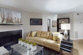 This single-floor residence offers a thoughtfully designed open layout that seamlessly connects the main living areas. The living room serves as the heart of the home, centered around a classic fireplace with a dark surround and complemented by plush carpeting, recessed art wall space, and generous natural light filtering through large windows dressed with floor-length curtains. A peninsula with dark granite countertops and white cabinetry bridges the living area to the kitchen, which features stainless steel appliances including a dishwasher, range, and microwave, all set against crisp white raised-panel cabinetry and warm wood-tone flooring. The dining area accommodates a full-sized table for multiple guests and includes a chandelier overhead and a decorative built-in ledge along the wall. The primary bedroom is generously proportioned with multiple windows, soft carpeting, and ample room for a sitting area. The bathroom includes a wide vanity with dark granite countertops, white cabinetry, a built-in makeup area with a stool, and a well-lit mirror. A dedicated laundry room houses a full-sized washer and dryer on wood-tone flooring, adding everyday practicality to this well-rounded residence.