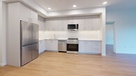 Located at 1100 McCallum Rd in Langford, BC, this thoughtfully designed two-bedroom, two-bathroom unit offers a clean, contemporary aesthetic throughout its single-floor layout. Light hardwood flooring and crisp white walls run consistently through the space, creating a bright and cohesive atmosphere accentuated by recessed pot lighting.

The open-concept kitchen and living area serves as the heart of the unit. The kitchen is equipped with full-height grey cabinetry, white quartz countertops, stainless steel appliances including a gas range, built-in dishwasher, refrigerator, and over-the-range microwave, all complemented by a subway tile backsplash.

Two generously sized bedrooms provide comfortable retreats, with the primary bedroom featuring a dedicated walk-through closet with wire shelving that leads directly into a private ensuite. The ensuite bathroom includes a wood-toned vanity with white quartz countertop, a soaker tub, and tile flooring. A second full bathroom serves the remainder of the unit.

Additional highlights include a versatile den, a dedicated laundry area, and two private balconies — one of which offers expansive views of the surrounding wetlands, treetops, and distant mountain ridgeline. A wall-mounted climate control unit ensures year-round comfort.