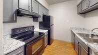 Located at 1300 Longcreek Dr in Columbia, SC, this single-floor unit offers a thoughtfully laid-out interior with a blend of hardwood-style flooring and plush carpeting across its living spaces. The entryway welcomes you with soaring vaulted ceilings and opens into a comfortable living area featuring a ceiling fan with light fixture, vertical blinds, and access to additional rooms. The kitchen is well-appointed with gray shaker-style cabinetry, granite-look countertops, black appliances including an electric range and refrigerator, a stainless steel dishwasher, and a range hood — all set atop warm hardwood-style flooring with a textured ceiling above. A pass-through counter connects the kitchen to the adjacent living or dining area, enhancing the open feel. The carpeted bedrooms are generously sized, with ample natural light from multiple windows fitted with blinds. The bathroom is finished with a gray vanity, granite-look countertop, mirrored medicine cabinet, and a tiled tub-shower combination, complemented by hardwood-style flooring. Throughout the unit, neutral wall tones and consistent updated finishes create a clean, cohesive aesthetic.