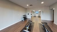 Located at 300 Hickory Hollow Pl in Nashville, Tennessee, this single-floor fitness center offers a clean, modern environment designed to support a variety of workout routines. The space is finished with durable wood-look flooring throughout, neutral gray walls, and white baseboards that give the facility a bright, contemporary aesthetic.

The layout is divided into distinct functional zones. A strength training area features a multi-tiered dumbbell rack stocked with a range of free weights, along with an adjustable workout bench and additional strength equipment. Adjacent to this is a dedicated cardio and cycling zone, where stationary bikes are positioned on protective floor mats. A wall-mounted flat-screen display serves as a focal point in the cycling area, ideal for guided workout programming.

A separate stretching and flexibility zone houses multiple stability and medicine balls in a range of sizes, alongside yoga mats, providing ample space for floor exercises and mobility work. Recessed and panel lighting ensures the entire facility is well-lit throughout.

Notably, the space benefits from large sliding glass doors and an adjacent door that open to an outdoor terrace, introducing natural light and providing direct exterior access. The terrace offers open views of the surrounding Nashville landscape, enhancing the overall workout environment with fresh air and natural brightness.