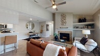 This single-floor home offers a thoughtfully designed layout with a warm, modern aesthetic throughout. The living room serves as the centerpiece of the space, boasting soaring vaulted ceilings, a ceiling fan, and a striking stone-surround fireplace with a white mantel. Herringbone-patterned hardwood-style flooring flows throughout the main living areas, complemented by large windows that invite generous natural light. Built-in shelving flanks the fireplace, providing both storage and display space, while an adjacent dining area with a round mirror adds an elegant touch.

The galley-style kitchen is efficiently arranged with crisp white cabinetry, light countertops, stainless steel appliances, and a deep sink — offering ample workspace and storage for everyday living.

The bedrooms feature plush carpeting and vaulted ceilings, with large windows that brighten each room. The primary bedroom includes access to a spacious walk-in closet. Additional bedrooms are well-sized and versatile.

The bathrooms are clean and functional. One features herringbone tile flooring, a white vanity, and decorative round mirrors, while the second includes an extended countertop with a large wall mirror, offering practical vanity space.

Throughout, the neutral color palette and cohesive design create a comfortable and inviting atmosphere.