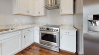 Located at 3501 Patterson Ave in Richmond, Virginia, this single-floor unit offers a thoughtfully designed layout with contemporary finishes throughout. Rich, dark hardwood-style flooring runs consistently across the living areas and bedrooms, creating a warm and cohesive aesthetic that contrasts beautifully with the neutral, light-toned walls.

The main living area is generously proportioned, bathed in natural light through multiple windows fitted with white horizontal blinds. Views of the surrounding neighborhood greenery are visible from these windows, adding a pleasant outdoor connection to the interior. A decorative pendant light fixture anchors the space.

The kitchen is well-equipped, featuring white shaker-style cabinetry, granite countertops, a stainless steel professional-grade range, and a sleek glass canopy range hood — a standout feature for cooking enthusiasts.

Bedrooms continue the hardwood flooring theme, with one bedroom offering a ceiling fan and a dedicated closet with built-in rod storage. Another bedroom includes a window with natural light and ample wall space.

Two bathrooms serve the unit. One includes a white vanity with granite countertop and a glass-enclosed walk-in shower with white subway tile accented by a dark tile border. The second bathroom mirrors the refined aesthetic with a tub/shower combination, similarly tiled, and a matching vanity. Both feature neutral large-format floor tiles.