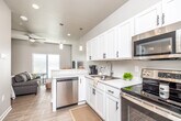 This single-floor unit offers a well-designed, open-concept layout that maximizes functionality within a compact footprint. Light wood-tone flooring runs consistently throughout, contributing to a bright, cohesive aesthetic. Neutral gray and white walls keep the space feeling airy and clean.

The kitchen is outfitted with white shaker-style cabinetry featuring matte black hardware, light marble-style countertops, and a full suite of stainless steel appliances including a range, over-the-range microwave, dishwasher, and refrigerator. Pendant lighting above the peninsula adds a contemporary touch, while the open sightlines connect the kitchen directly to the living area.

The living and sleeping area is combined within a single open space, with large windows dressed in horizontal blinds allowing substantial natural light. A ceiling fan overhead adds comfort and practicality.

The bathroom features a single-sink vanity with white cabinetry, a large mirror, white countertops, and a full tub-shower combination with a curtain rod. Light wood-tone flooring continues here as well.

The entryway is clean and functional, with a modern front door, an adjacent interior door, and neutral walls that set a welcoming tone upon entry.