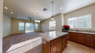 Located at 1800 Wisdom Way in Modesto, California, this single-story home offers a thoughtfully designed, open-concept layout filled with natural light. A welcoming hallway with light wood-style flooring leads into the heart of the home, where the kitchen and living area flow seamlessly together. The kitchen is a standout, showcasing warm medium-toned wood cabinetry, granite countertops, a generously sized center island with pendant lighting, and a full suite of stainless steel appliances including a refrigerator, range, microwave, and dishwasher. A double sink with a window view completes the workspace. The adjacent living area features plush carpeting, a ceiling fan, and a chandelier, with sliding glass doors that invite ample natural light and outdoor access. Bedrooms are carpeted and well-proportioned, with closet space including a walk-in option with built-in shelving and hanging rods. Bathrooms are finished with granite-topped wood vanities and light wood-style flooring. The dedicated laundry room includes top-load washer and dryer units, upper cabinetry, and a granite-topped utility sink. An attached garage provides additional storage and parking. Throughout, the home maintains a clean, neutral palette that enhances its bright and welcoming atmosphere.