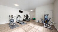Located at 1637 Marakanda Trail in Sugar Hill, Georgia, this fitness facility is a compact yet comprehensively outfitted exercise space spread across a single floor. The interior is finished with light wood-style flooring throughout, crisp white walls, and flush-mount ceiling lighting that creates a clean, bright atmosphere. Natural light filters in through multiple windows fitted with horizontal blinds, further enhancing the open and airy feel of the space.

The main exercise room is organized to accommodate a diverse range of workout activities. Cardio equipment includes multiple treadmills and an elliptical machine, each positioned on protective floor mats. A stationary bike provides an additional low-impact option. For strength training, a multi-function cable machine serves as the focal point, accompanied by a dedicated dumbbell and kettlebell rack displaying a full range of colorful weights. A wall-length mirror spans one side of the room, amplifying the sense of space and allowing users to monitor their form. Stability balls, medicine ball racks, and a foam roller round out the functional training accessories. A wall-mounted television adds an entertainment element. The entrance provides a clear transition into the workout area, with a hand sanitizer dispenser visible near the entry point.