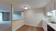 This single-floor, 2-bedroom, 1-bathroom unit offers a practical and comfortable layout designed for everyday living. The kitchen is well-equipped with white cabinetry, granite-style countertops, a stainless steel sink, a dishwasher, and an electric range. Under-cabinet lighting enhances the workspace, while hardwood-style flooring flows throughout the kitchen and dining area. A pass-through window connects the kitchen to the adjacent living space, promoting an open feel between the two areas. The living room is generously sized, featuring plush carpeting, a coat closet, and a sliding glass door that opens to a private balcony with views of surrounding greenery. Baseboard heating is present throughout the unit, ensuring consistent warmth. Both bedrooms are carpeted and offer a comfortable, quiet retreat, with the primary bedroom featuring dual windows that bring in natural light and views of the outdoors, along with a wall-mounted air conditioning unit. The shared bathroom is clean and functional, featuring tile flooring, a combined tub and shower with a white surround, a toilet, and a vanity with under-sink storage. Neutral wall tones and textured ceilings carry throughout the unit, creating a cohesive and move-in-ready environment.