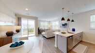 This single-floor residence at 2300 Reservoir Ave in Trumbull, Connecticut, offers a thoughtfully designed open-concept layout finished with light hardwood-style flooring throughout the main living areas. The kitchen serves as a central hub of the space, featuring gray shaker-style cabinetry, a white quartz peninsula with bar seating, stainless steel appliances including a refrigerator, range, and dishwasher, a subway tile backsplash, and stylish pendant lighting overhead. The kitchen flows seamlessly into a bright living area filled with natural light from multiple windows and a sliding glass door that opens onto a private balcony with outdoor views.

Two bedrooms provide comfortable retreats; one features wooded views through a large window, while the other offers a quiet, softly lit atmosphere with plush carpeting. The primary bathroom includes a walk-in glass-enclosed shower with white subway tile, a gray vanity with quartz countertop, and wood-look flooring. A second bathroom mirrors the clean, contemporary aesthetic with a matching vanity and efficient layout. A dedicated in-unit laundry closet with a stacked washer and dryer adds everyday convenience. The overall ambiance is modern, bright, and well-appointed throughout.