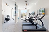Located at 375 Gartrell St SE in Atlanta, GA, this fitness center offers a comprehensive exercise environment designed to support a wide range of workout routines. The single-floor space is thoughtfully laid out to maximize usability while maintaining an open, airy feel. Bright white walls, carpeted flooring, and multiple ceiling fans contribute to a clean, comfortable atmosphere throughout.

Large windows along the perimeter flood the space with abundant natural light and frame views of the surrounding Atlanta neighborhood, creating an energizing environment. A decorative column with bold blue and white horizontal stripes serves as a striking visual focal point that divides the cardio and functional training zones.

The cardio section is well-appointed with multiple Star Trac treadmills, elliptical trainers, and stationary bikes, each accompanied by wall-mounted flat-screen televisions for entertainment during workouts. A dedicated strength training area features a multi-functional cable and weight machine, complemented by a full dumbbell rack and adjustable bench. A separate room, enclosed with glass-panel doors, provides additional space for focused training or stretching. Stability balls in various sizes and a leg extension machine round out the diverse equipment offerings.

Overall, this fitness center delivers a bright, modern, and fully equipped workout facility suitable for a broad spectrum of fitness needs.