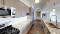 This contemporary single-floor residence showcases a thoughtfully designed open layout with high-end finishes throughout. The space features two distinct kitchen configurations: one with a generous island topped with granite countertops, pendant lighting, sleek taupe cabinetry, and stainless steel appliances including a gas range and refrigerator; and a second galley-style kitchen equally well-appointed with matching stone counters, tile backsplash, and an in-unit stacked washer and dryer nearby for added convenience.

The living area is bright and welcoming, finished with dark hardwood flooring, a ceiling fan, and dual sliding glass doors that open onto a private wraparound deck. This outdoor space features warm wood decking and elevated urban views of the surrounding cityscape. Multiple bedrooms are carpeted and filled with natural light through large windows overlooking the city. One bedroom connects directly to a primary bathroom featuring a wide vanity, tiled soaking tub, and an adjacent walk-in closet. A second full bathroom offers a tiled tub-shower combination with built-in shelving. The overall aesthetic is clean, modern, and move-in ready.