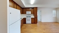 This single-floor residence offers a clean, functional layout with a bright and welcoming atmosphere throughout. The open living area features warm hardwood-style flooring and is filled with natural light from large windows fitted with blinds, creating an airy feel. A door leads directly to a private balcony, providing a convenient outdoor extension of the living space with views of the surrounding neighborhood.

The kitchen is well-appointed with rich, warm-toned wood cabinetry extending to the ceiling for ample storage, white appliances including a gas range, over-the-range microwave, and refrigerator, complemented by light countertops and a recessed ceiling with overhead lighting. The hardwood-style flooring continues seamlessly from the living area into the kitchen.

The bedroom features plush carpeting, crisp white walls, and a wide window that invites natural light. A full-width mirrored sliding closet adds both practicality and a sense of spaciousness to the room.

The bathroom is neatly finished with tile flooring, a wood-toned vanity with a white countertop and integrated sink, a large wall mirror, and a well-lit vanity light fixture above, maintaining the clean and consistent aesthetic found throughout the home.