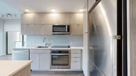 Located at 301 M St SW, Unit 503 in Washington, DC, this two-bedroom, one-bathroom residence offers a well-designed layout with a clean, contemporary aesthetic. The modern kitchen is a standout feature, outfitted with light wood-grain cabinetry extending to the ceiling, stainless steel appliances including a refrigerator, electric range, built-in microwave, and dishwasher, along with light quartz countertops and a subtle tile backsplash. Wood-look flooring runs throughout the unit, lending warmth and continuity across spaces. The living and dining areas are positioned to maximize the flow of the home, with a glass partition wall adding an architectural element that allows natural light to pass between rooms. Both bedrooms are well-proportioned, each featuring large windows with roller shades that frame views of the surrounding greenery. Exposed concrete columns add an industrial character that contrasts nicely with the otherwise soft, neutral palette. The bathroom is finished with large-format light tile flooring, a wall-mounted vanity with mirror, and a glass-enclosed walk-in shower. Additional highlights include in-unit laundry, three closets for ample storage, and a private balcony — a rare outdoor amenity in the heart of the city.