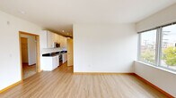 This contemporary single-floor unit offers a thoughtfully designed layout that balances functionality and modern aesthetics throughout. Light hardwood-style flooring runs seamlessly through the main living areas, kitchen, and bathroom, creating a cohesive and clean visual flow.

The open living area is bright and airy, benefiting from large windows and sliding glass doors that lead to a private balcony. The outdoor space provides views of the surrounding urban environment, while a wall-mounted mini-split system ensures year-round climate comfort.

The kitchen is efficiently laid out in a galley-style configuration, featuring white gloss cabinetry with sleek hardware, dark granite countertops, a stainless steel sink, and a full suite of stainless steel appliances including a refrigerator, range, microwave, and dishwasher. Recessed lighting illuminates the space effectively.

The bedroom is carpeted for warmth and comfort, with a large window that brings in natural light and urban views. It is complemented by a generously sized walk-in closet outfitted with wire shelving, as well as an additional sliding-door closet for further storage.

The full bathroom includes a tub-shower combination, a white vanity with dark countertop, a large mirror, and matching hardwood-style flooring. Light-toned wood door frames and trim throughout add a warm architectural accent to the unit's modern palette.