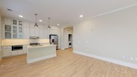 Located at 600 Caraway Crossing in Chapel Hill, NC, this single-floor residence offers a thoughtfully designed open-concept layout filled with natural light and clean, contemporary finishes throughout. The living and dining area features light hardwood-style flooring, crown molding, recessed lighting, and a ceiling fan, with large windows fitted with blinds that invite abundant natural light into the space.

The kitchen is a standout feature, showcasing floor-to-ceiling white shaker cabinetry with glass-front upper cabinets, a textured white tile backsplash, and light countertops. A central island with pendant lighting provides additional workspace and serves as a natural gathering point. Stainless steel appliances, including a French door refrigerator, electric range, and built-in microwave, complete the well-appointed kitchen. A dedicated laundry area with a washer is conveniently accessible just off the main living space.

The bedrooms are carpeted for comfort and feature neutral wall tones and windows overlooking the surrounding neighborhood. One bedroom includes an en-suite bathroom and a walk-in closet with built-in shelving, while an additional bedroom is served by a nearby full bathroom. The overall ambiance is bright, clean, and move-in ready, with a cohesive neutral palette that lends versatility throughout every room.