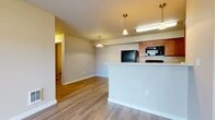 Located at 12928 E Mansfield Ave in Spokane Valley, WA, this single-floor unit offers a functional and well-organized layout across four bedrooms and two full bathrooms. The open living area features warm-toned luxury vinyl plank flooring and neutral walls, creating a bright and clean atmosphere. A peninsula-style kitchen anchors the space, equipped with warm wood cabinetry, light countertops, black appliances including a refrigerator, range, microwave, and dishwasher, and pendant lighting overhead — all arranged in an efficient galley configuration. The living room is lit naturally through a sliding glass door dressed with vertical blinds, offering access to an outdoor area. The bedrooms are carpeted for comfort, finished with neutral tones and panel-style doors. Both bathrooms feature warm wood vanities, light countertops, large mirrors, and vinyl plank flooring, with one bathroom offering additional open shelving for storage. A dedicated laundry room houses a full-size washer and dryer with overhead wire shelving. A utility room provides additional functional space. Throughout the unit, clean white trim, consistent finishes, and a straightforward floor plan contribute to a practical and comfortable living environment.