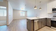 This single-floor unit features a clean, contemporary design with a neutral color palette and light wood-style flooring flowing throughout the main living areas. The open-concept kitchen serves as the centerpiece of the space, showcasing a two-tone cabinet scheme with gray lower cabinets and crisp white upper cabinets, paired with a white quartz countertop. A peninsula island with an undermount sink provides additional prep space and is accented by brushed nickel pendant lights. A full suite of stainless steel appliances includes a refrigerator, range, microwave, and dishwasher.

The living area extends naturally from the kitchen, bathed in natural light from a window fitted with horizontal blinds. The bedrooms offer a comfortable retreat, with some featuring plush carpeting and windows for natural light, while others continue the wood-style flooring. The primary bathroom is well-appointed, featuring a glass-enclosed walk-in shower with tile surround, gray vanity cabinetry with white countertop, and direct access to a walk-in closet. Throughout the unit, the consistently modern finishes and light, airy atmosphere create a cohesive and inviting living environment.